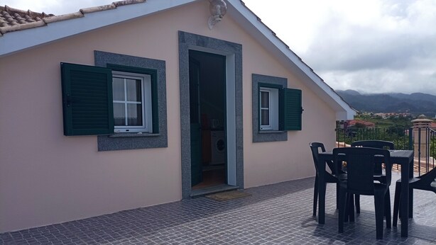 A building with a tiled roof, two windows with green shutters, and a patio area with a table and chairs. - Guest Apartment in Santana (Santana)