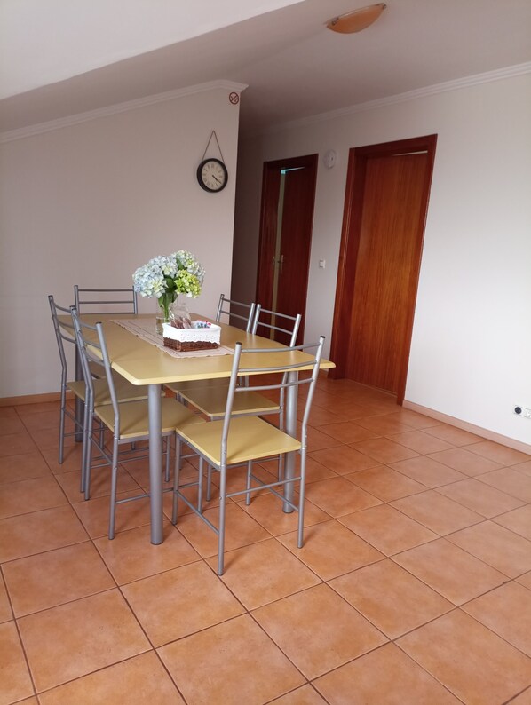 A dining area with a table and chairs, a clock on the wall, and a door in the background. - Guest Apartment in Santana (Santana)