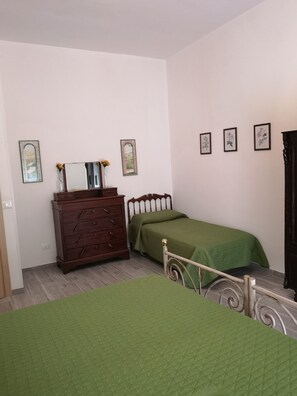 Une chambre à coucher avec une commode en bois, un lit recouvert d’une couverture verte et trois tableaux encadrés accrochés au mur.