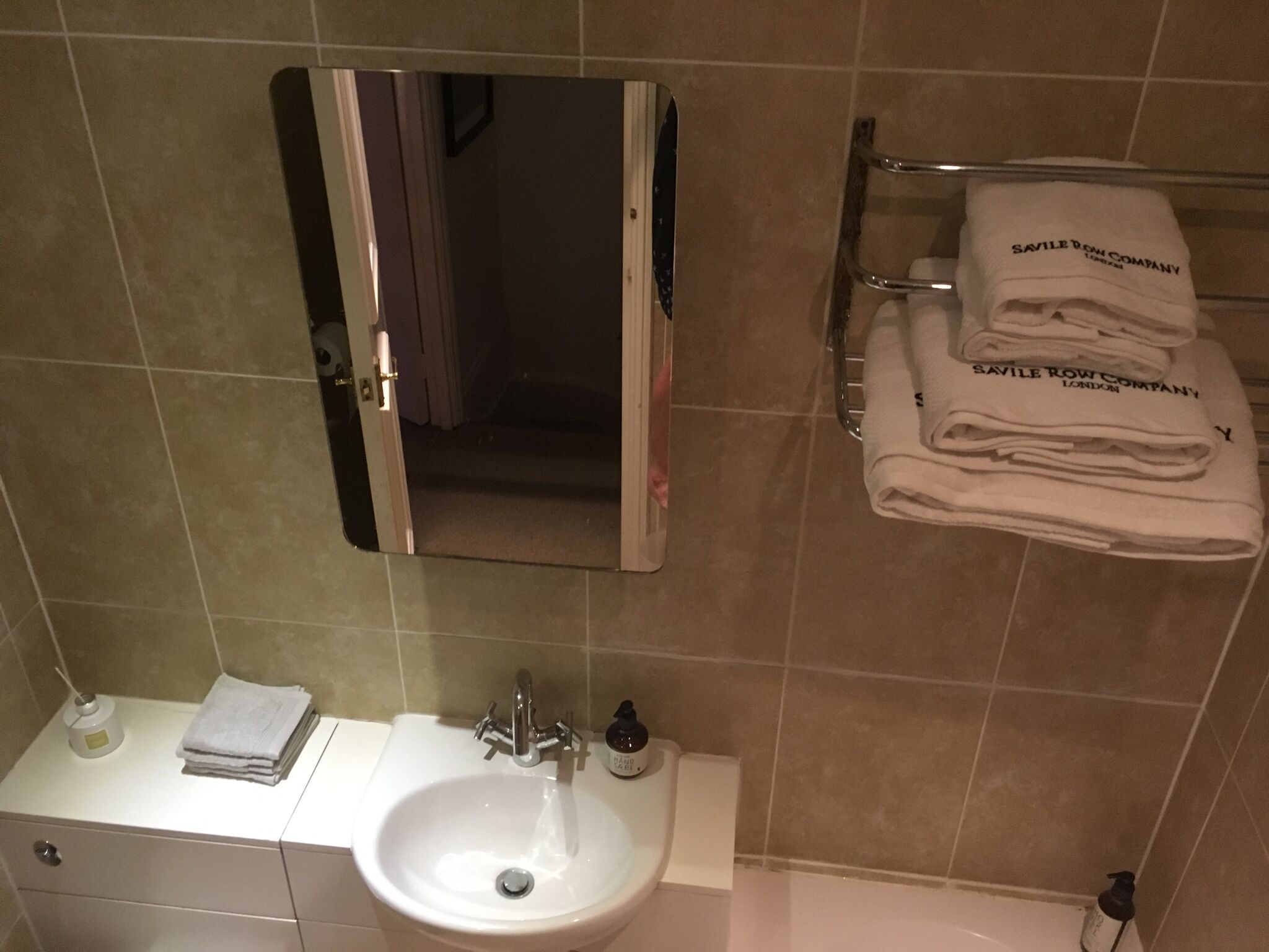 A bathroom with a sink, mirror, towel rack, and a bottle of hand soap.