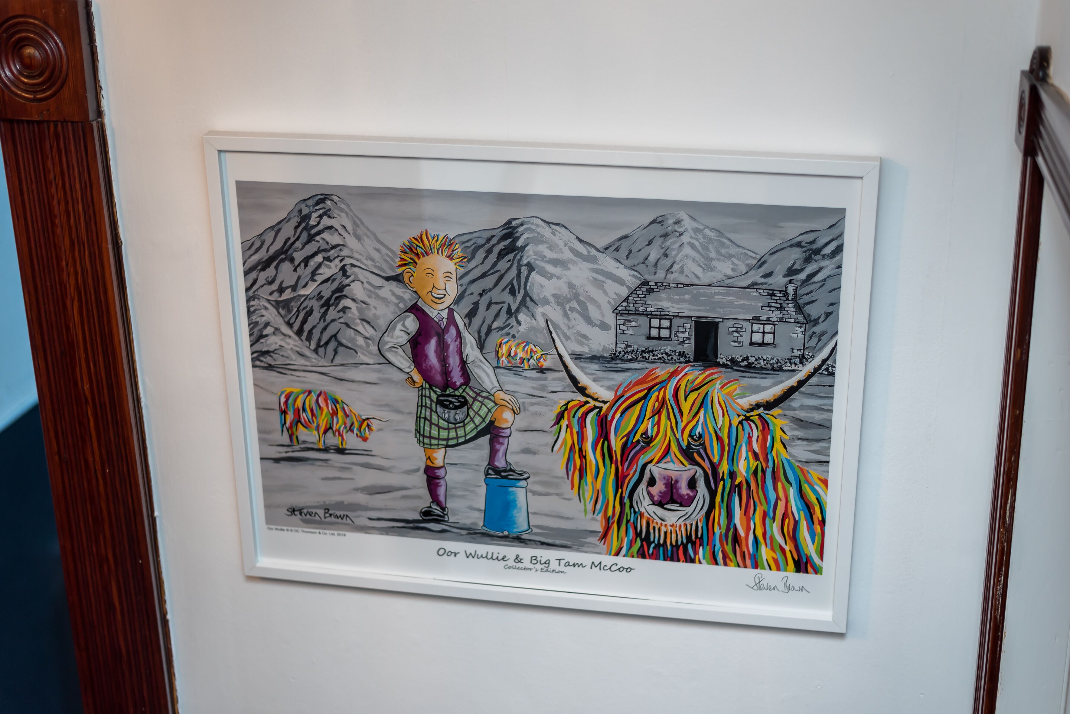 Obra enmarcada que muestra a una persona con un animal colorido, sobre un fondo montañoso, en una pared blanca.