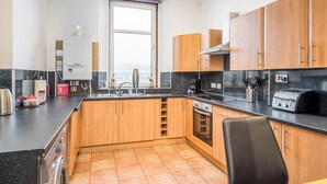 A modern kitchen with wooden cabinets, a built-in oven, a coffee machine, and a window with a view. - Claymore Apartment, Brook Street, central Broughty Ferry, Dundee (Dundee)
