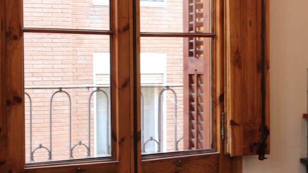 A wooden-framed window with a view of a brick building and a metal railing.