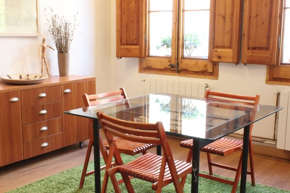 Un comedor con una mesa de vidrio y sillas de madera, un mueble de madera con cajones y una planta en maceta.
