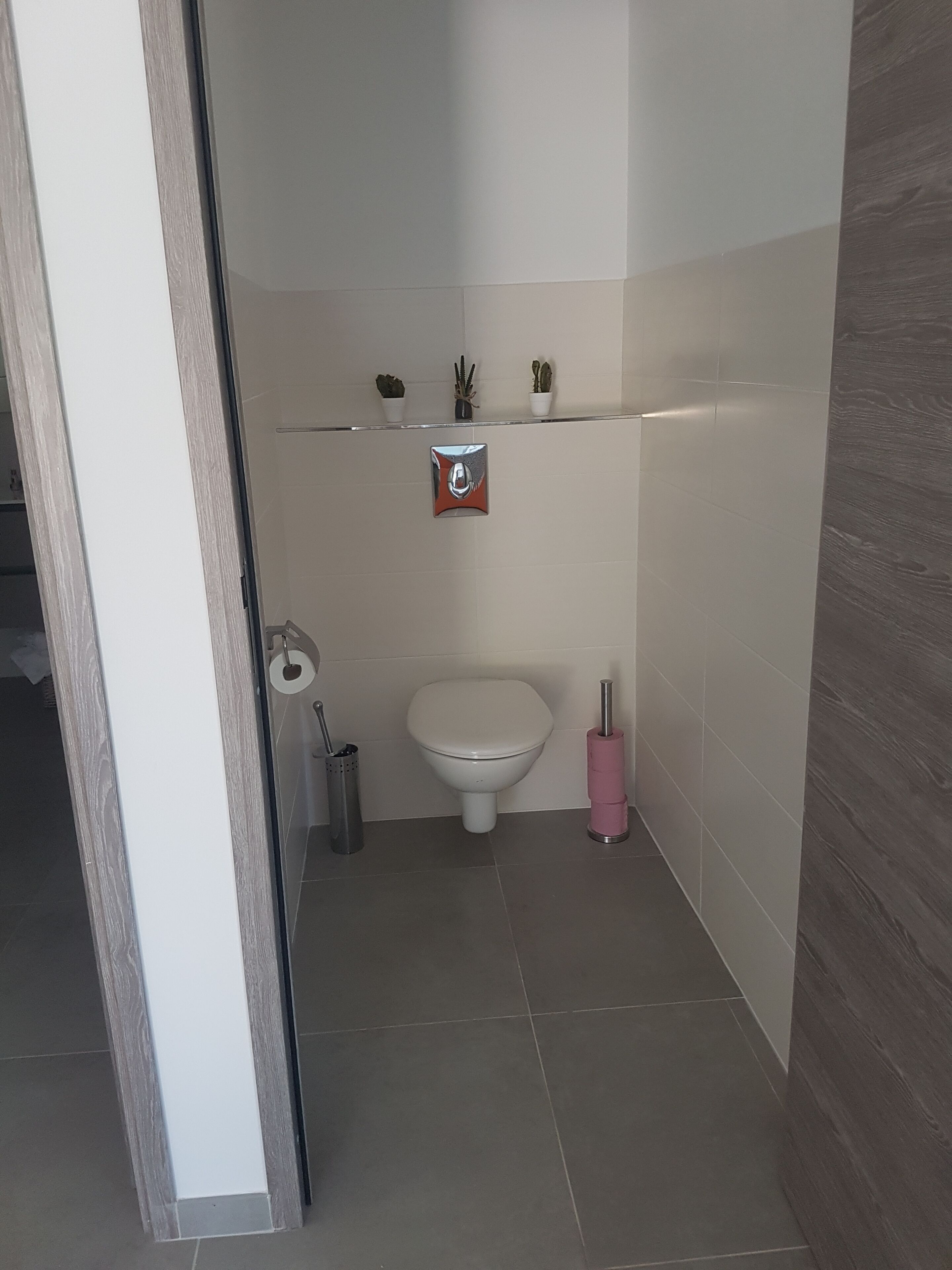 Un baño con inodoro, secamanos, cubo de basura y un estante con objetos decorativos.