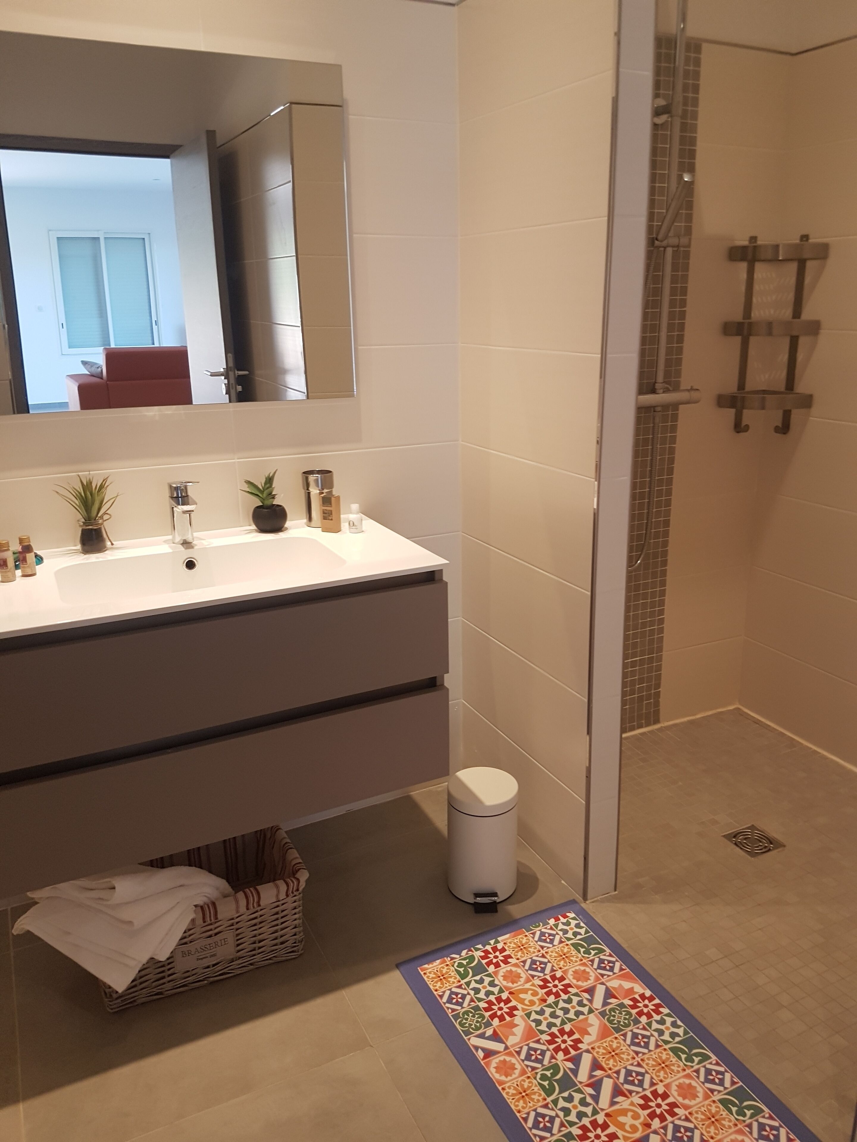 Een moderne badkamer met een witte wastafel, een glazen douchecabine en een kleurrijk, patroonrijk vloerkleed.