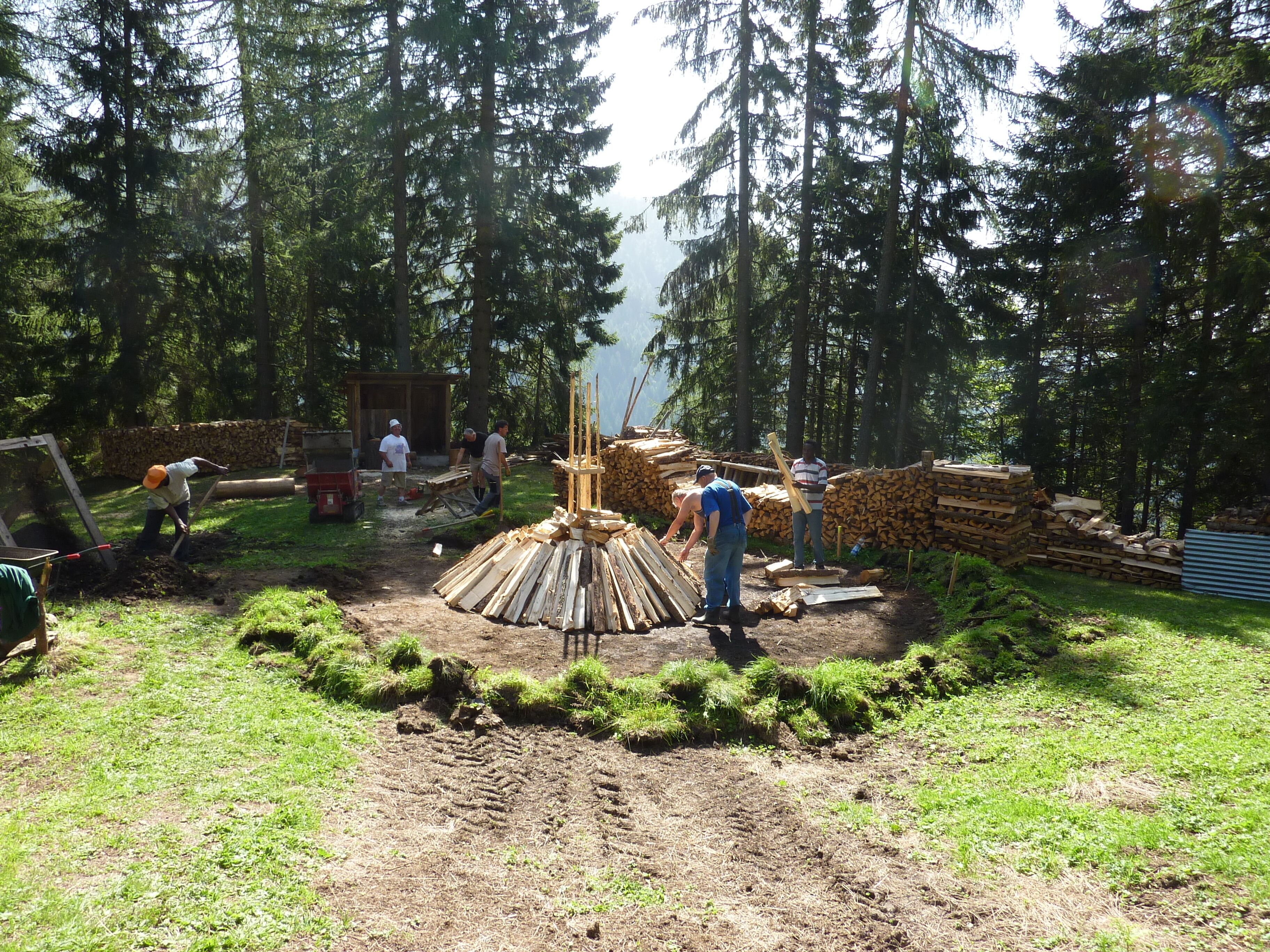 Een bouwplaats met werkmannen, houten planken en een stapel hout.