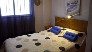 Een slaapkamer met een bed, nachtkastje, lamp, raam met gordijnen en een wandklok.