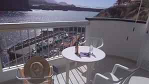 Een balkon met tafel en stoelen, met uitzicht op een jachthaven met boten en een kustlijn.