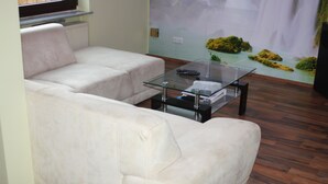 Un salon avec un canapé blanc, une table basse en verre et une fresque murale représentant une cascade.