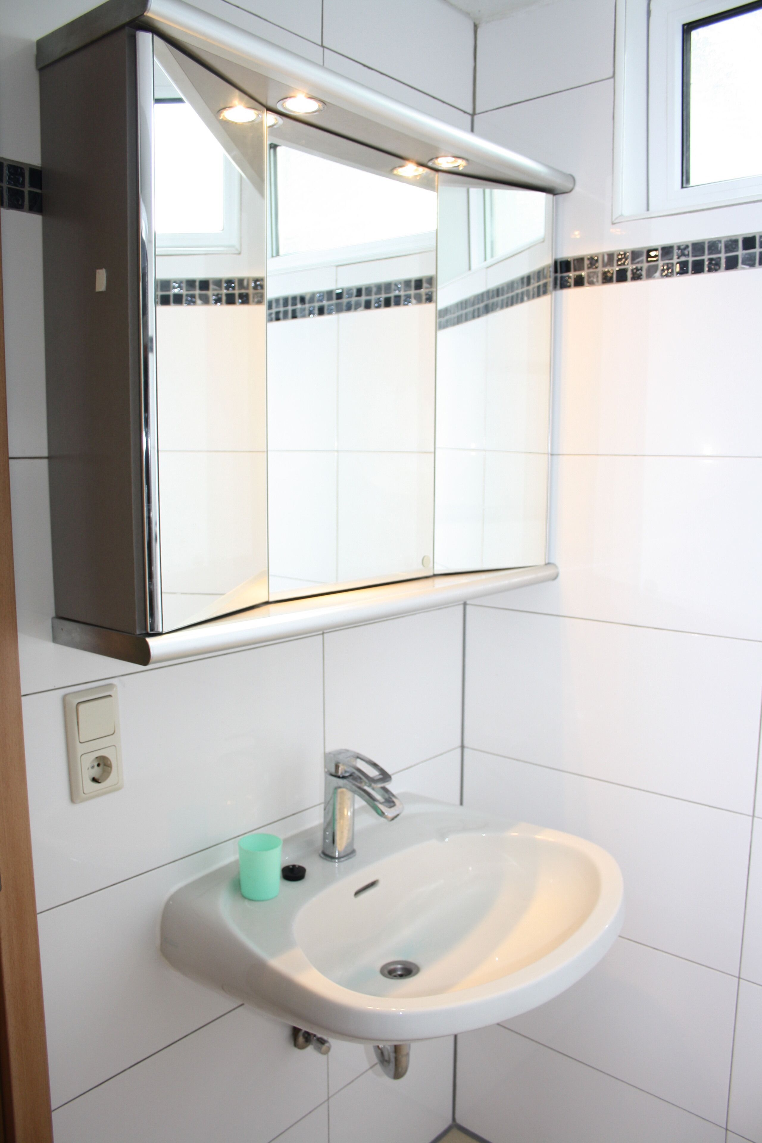 Un bagno con un lavandino bianco, uno specchio sopra e uno schienale piastrellato.