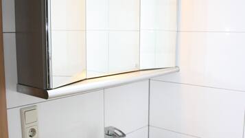 Un bagno con un lavandino bianco, uno specchio sopra e uno schienale piastrellato.
