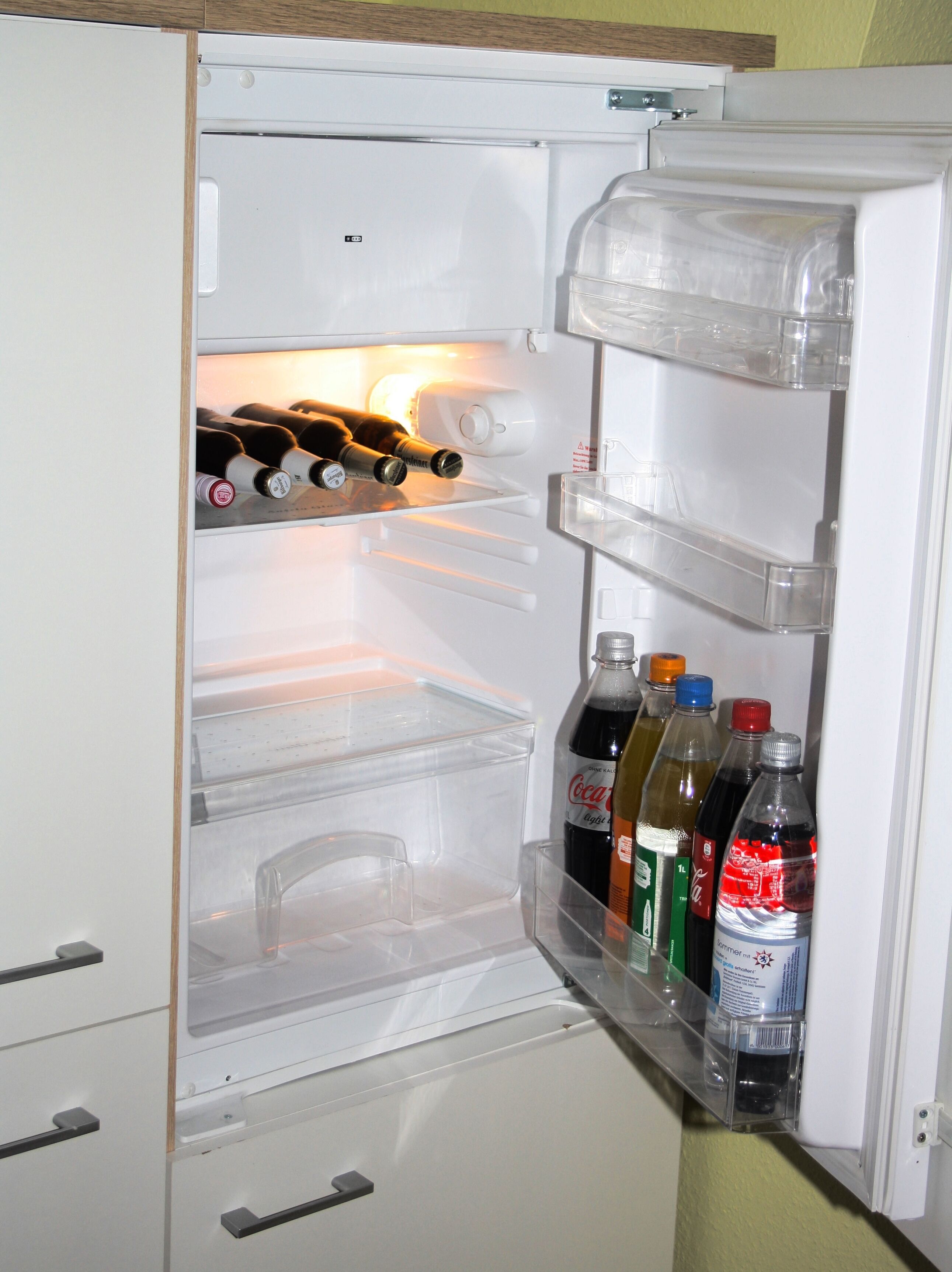 Un refrigerador abierto con estantes que contienen botellas de bebidas.