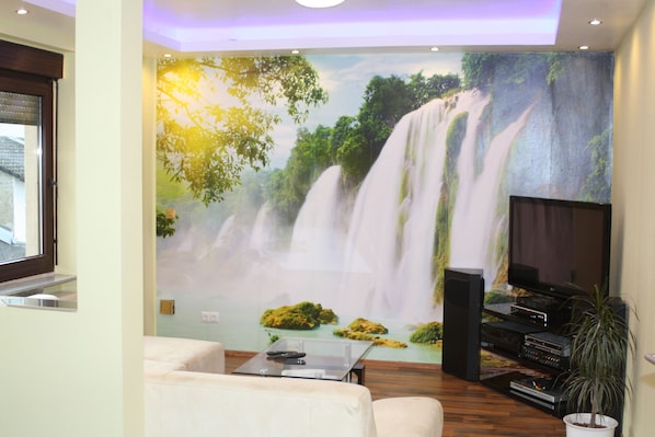 Un salón con un gran mural de una cascada, un televisor de pantalla plana y un sistema de sonido.