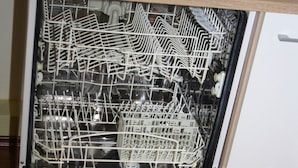 Un lave-vaisselle avec des étagères et des ustensiles à l’intérieur, un évier au-dessus et un plan de travail en bois en dessous.