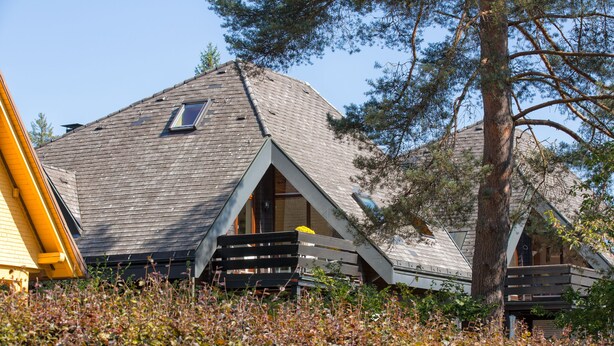 Ein Haus mit geneigtem Dach, einer Dachkuppel und einer Holzterrasse.