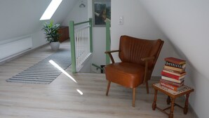 A room with a wooden floor, a brown leather chair, a small table with books, a potted plant, and a staircase with a green railing. - Art and the sea - close to everything (Varel)