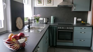 A modern kitchen with a sink, stove, and cabinets. There are two framed pictures on the wall, a vase with flowers on the counter, and a fruit basket. - Art and the sea - close to everything (Varel)
