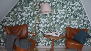 A room with two brown leather armchairs, a small wooden table with a book, and a floor lamp. The wall has a leafy pattern wallpaper. - Art and the sea - close to everything (Varel)