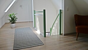 A room with a sloped ceiling, a green railing, a potted plant, a striped rug, and a wooden chair. - Art and the sea - close to everything (Varel)