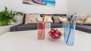 Drei Gläser mit unterschiedlich farbigen Strohhalmen und eine Schale Erdbeeren auf einem Tisch.