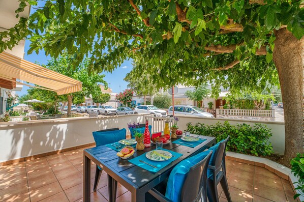 An outdoor dining area with a table set for two, surrounded by greenery and a view of parked cars. - House in Can Picafort Aurore near the beach (Can Picafort)
