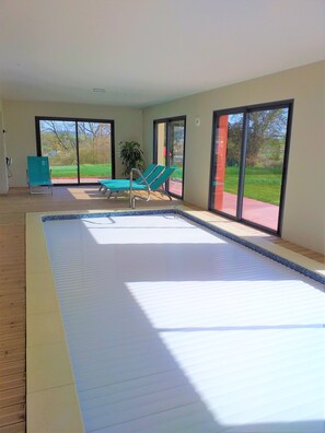 Une piscine intérieure spacieuse, dotée de grandes portes en verre qui donnent sur un jardin.