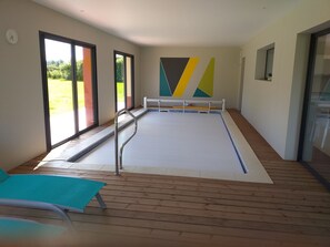 Swimmers can enjoy a rectangular pool surrounded by wooden flooring and large windows.