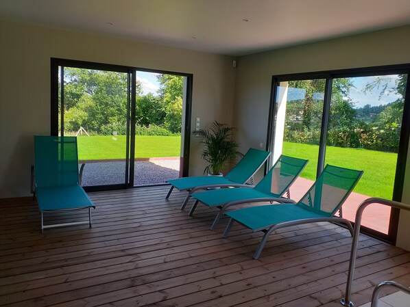 Une pièce dotée d’un plancher en bois, de quatre fauteuils verts confortables et de grandes portes-fenêtres coulissantes donnant sur un espace extérieur verdoyant.