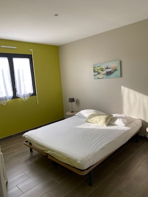A bedroom with a bed, a window with curtains, a bedside lamp, and a wall-mounted painting. - House with private indoor pool, heated year-round and not overlooked (Neufchâtel-en-Bray)