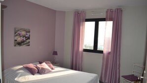 Un dormitorio con una cama, una mesita de noche, una lámpara, una ventana con cortinas y un aire acondicionado instalado en la pared.
