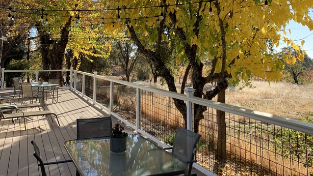 A deck with a glass table and chairs, surrounded by trees with yellow leaves, and a white fence.