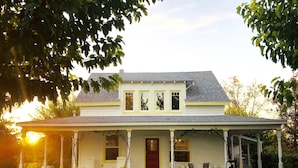 A two-story house with a porch, a front door, and a small front yard with grass and scattered leaves.