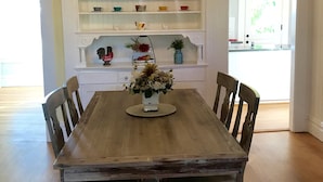 A dining room with a wooden table, six chairs, a chandelier, and a farmhouse sign on the wall.