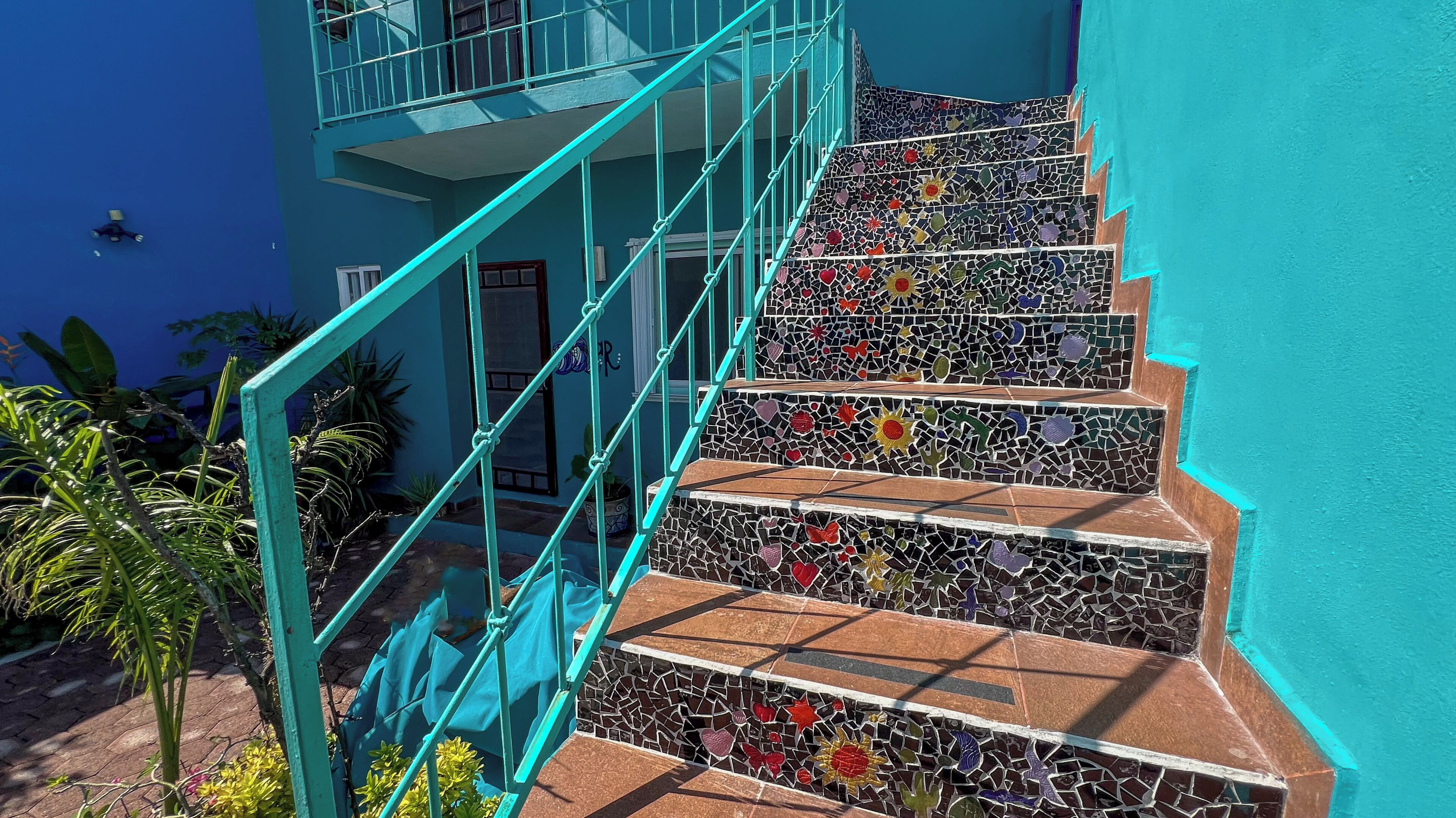 A staircase with turquoise railings and multicolored mosaic steps.