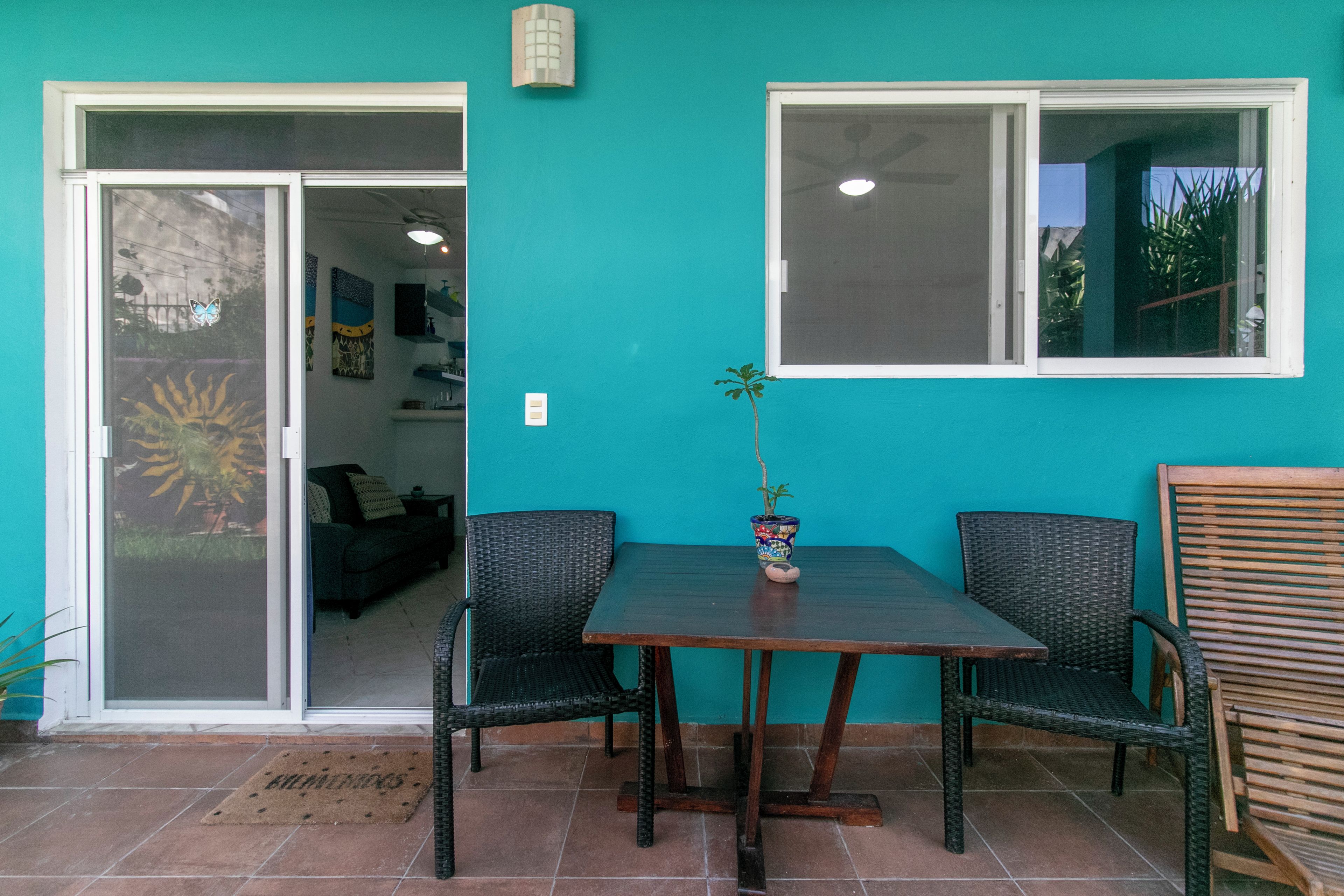 A patio with a table and chairs, a potted plant, and a sliding glass door leading to an interior space.