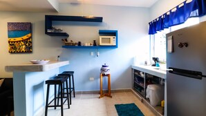 Una cocina compacta con encimera blanca, microondas, refrigerador y un valance azul a rayas.