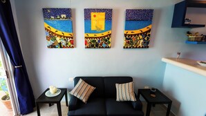 Una sala de estar con un sofá negro, dos mesitas auxiliares a juego y tres cuadros abstractos en la pared.