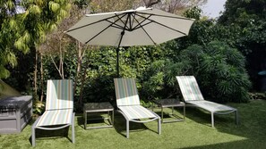 A patio area with three striped lounge chairs, a table, and a large umbrella.