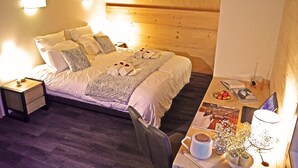Una habitació acollidora amb sostre de fusta, un llit ben arropat amb almoinos i una manta, una taula de nit amb una làmpada i un escriptori petit amb un ordinador portàtil i objectes decoratius.