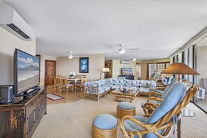 A spacious living room with a large sofa, wicker chairs, a television, and a dining area.