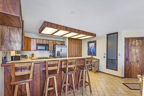 A kitchen with wooden bar stools, a large island, and modern appliances.