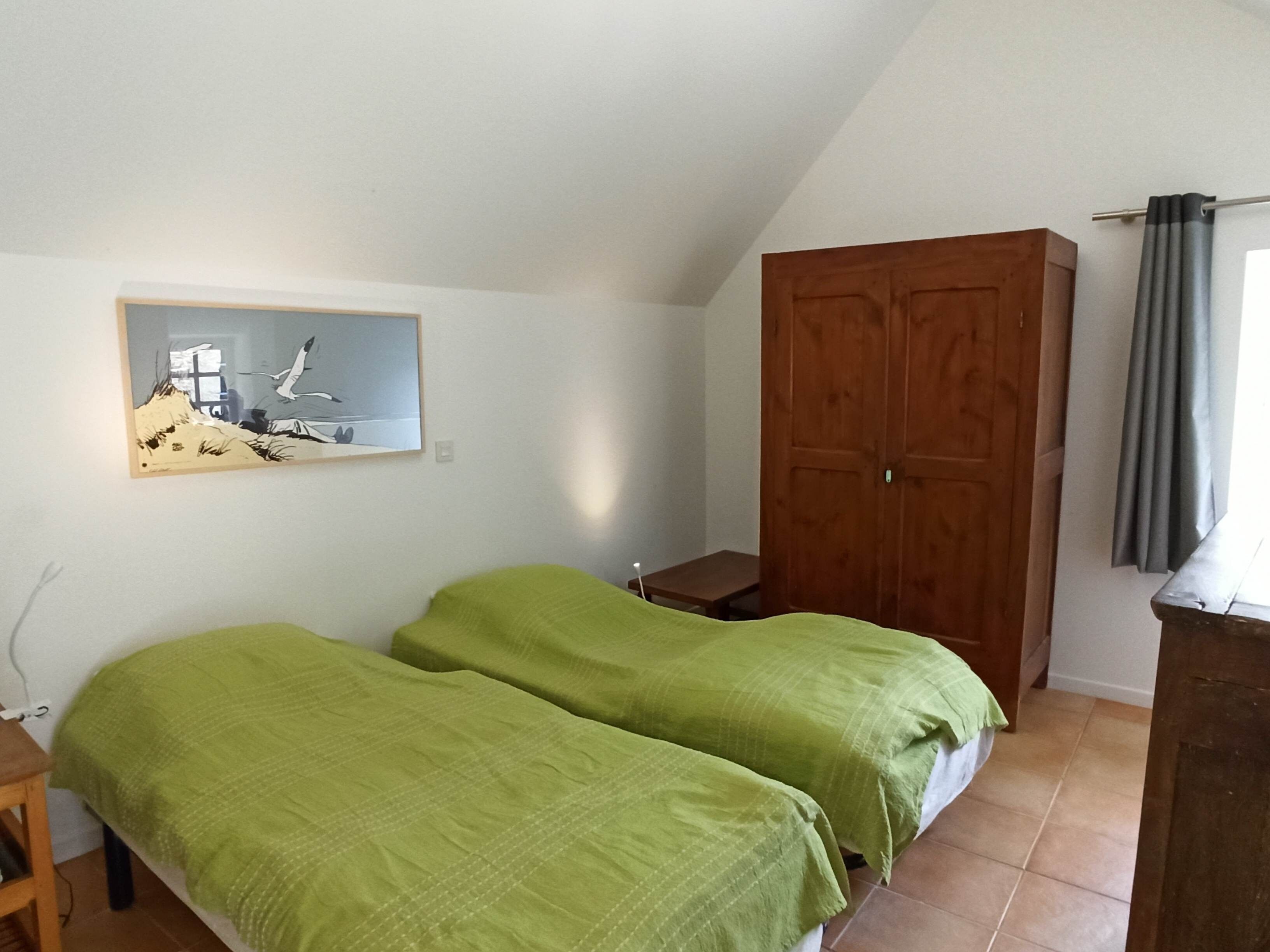 Una stanza con due letti, un armadio in legno, un quadro appeso e una finestra con tende.