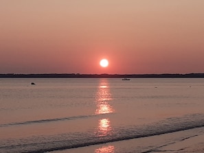 Tramonto sul mare calmo con una barca all'orizzonte.