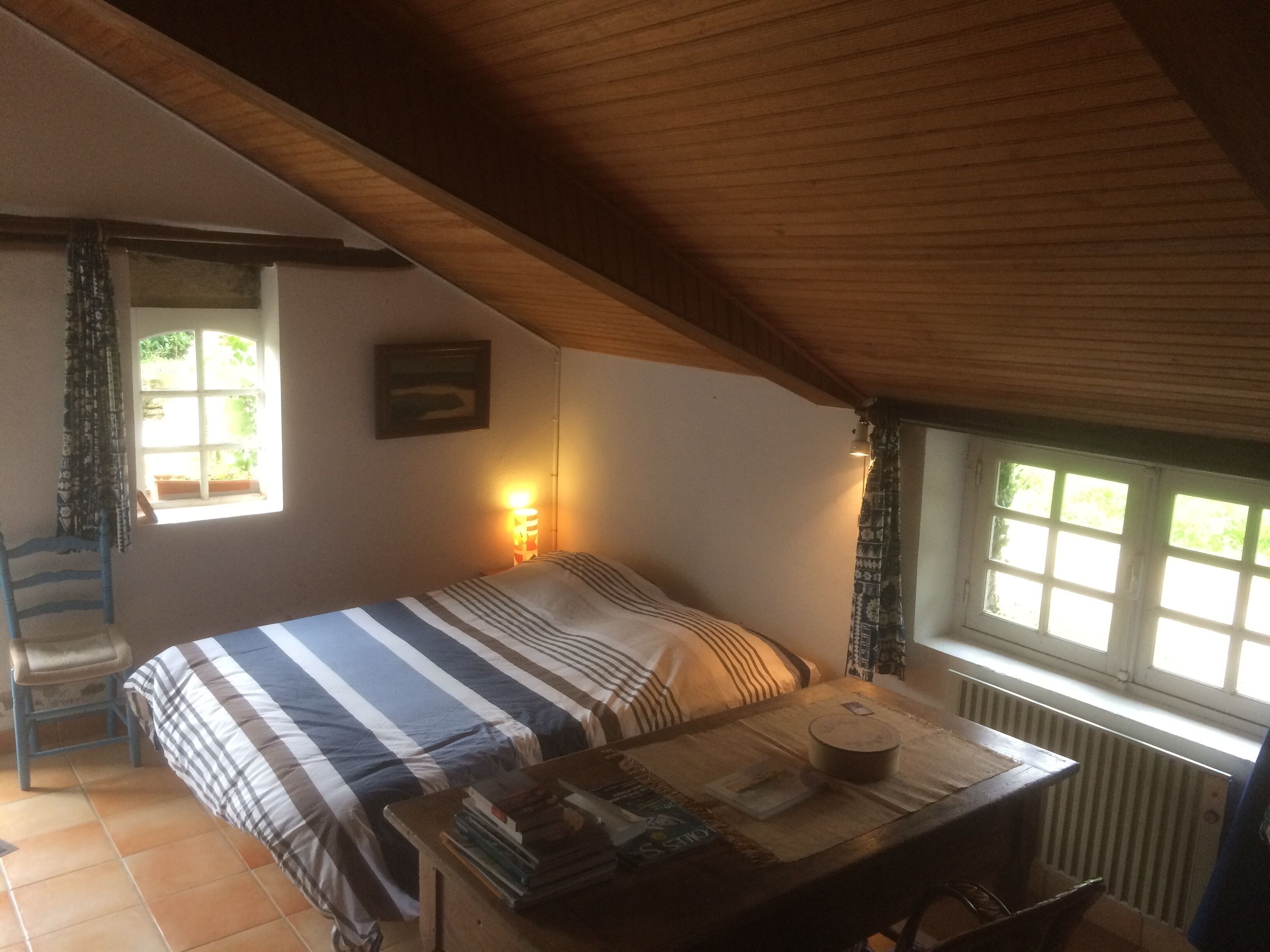 Un dormitorio con una cama, una mesa con libros, una ventana y un radiador.