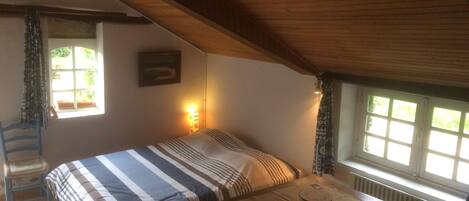 Un dormitorio con una cama, una mesa con libros, una ventana y un radiador.
