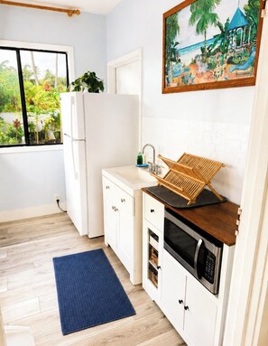 A compact kitchen with a built-in microwave, a sink with a wooden drying rack, and a window overlooking a garden.