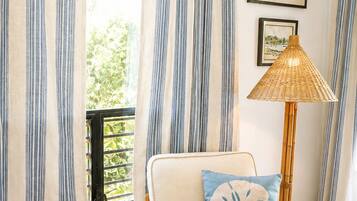 A room with a wicker chair, a small table with magazines, and a floor lamp.