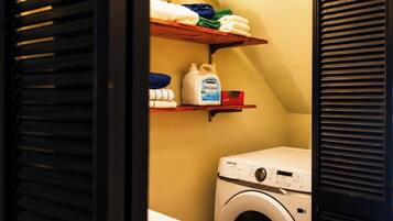 A laundry room with a washing machine, shelves with folded towels, and a bottle of laundry detergent.