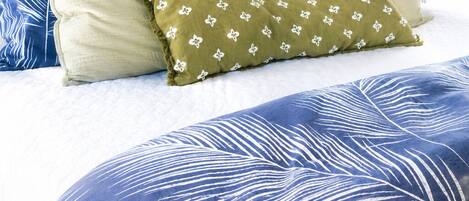 Un lit avec une couvre-lit aux motifs de feuilles bleues et blanches, deux oreillers aux mêmes motifs, et un tableau encadré au-dessus du lit.